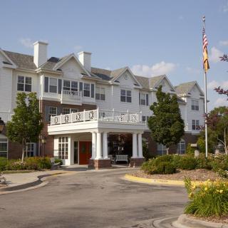 A large residential building with a landscaped entrance and flagpole on a sunny day.