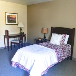 A minimalist bedroom featuring a single bed, desk, chair, and lamp.