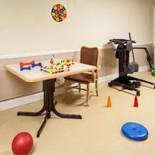 A room with exercise equipment, a table with toys, and various exercise items on the floor.