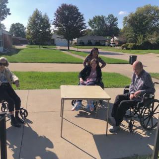 A group of people sitting in wheelchairs around a table outdoors on a sunny day.