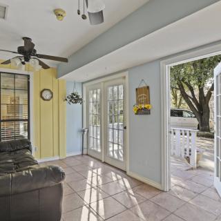 A bright living room with glass doors leading to an outdoor area, featuring a ceiling fan and tiled flooring.