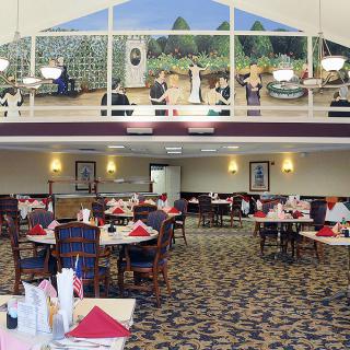 A spacious dining area with tables and chairs, featuring people enjoying their meals. A large mural decorates the wall above.
