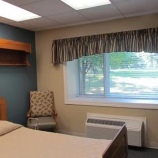 A simple bedroom with a bed, chair, and window letting in natural light.