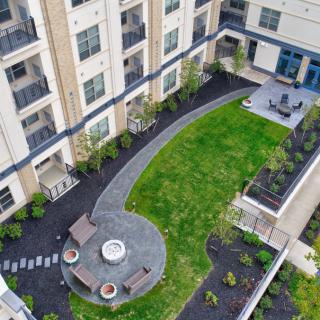Aerial view of a modern apartment complex courtyard featuring a green lawn and patio area with a fire pit.