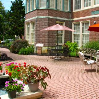 A charming outdoor patio with tables and umbrellas, surrounded by lush greenery and colorful flowers.