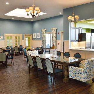 A well-lit dining area featuring multiple tables and chairs, with a view into the kitchen.