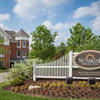 A view of a retirement community with well-maintained landscaping and a prominent entrance sign under a blue sky.