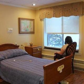 A woman sitting in a chair looking out of the window in a cozy bedroom.