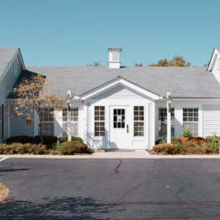 A charming residential building with a welcoming front entrance, surrounded by well-maintained landscaping on a clear day.