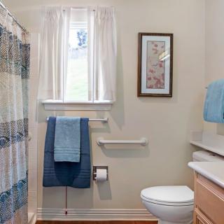 A clean and tidy bathroom with a shower curtain, window, towels, toilet, and a framed picture.