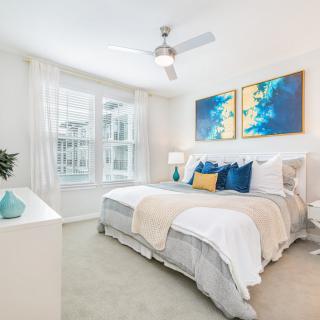 A modern and bright bedroom featuring stylish decor, vibrant artwork, and a cozy bed under a ceiling fan.