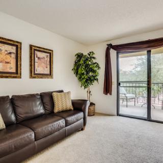 A cozy living room featuring a dark leather sofa, decorative artwork on the walls, and a view of the balcony through the sliding doors.