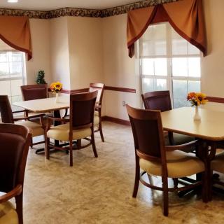 A cozy dining area with multiple tables and chairs, adorned with curtains and sunflowers.