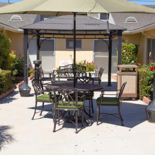A cozy outdoor seating area featuring a gazebo, dining table, and chairs surrounded by greenery.