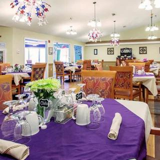 A well-decorated dining room with neatly arranged tables and chairs, featuring purple tablecloths and elegant lighting.