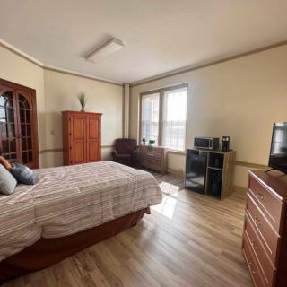 A spacious bedroom with wooden furniture, including a bed, dresser, and cabinet, featuring a large window and hardwood flooring.