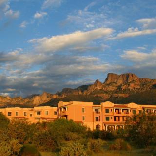 A resort building basking in the warm glow of a sunset, set against a backdrop of rugged mountains and desert landscape.