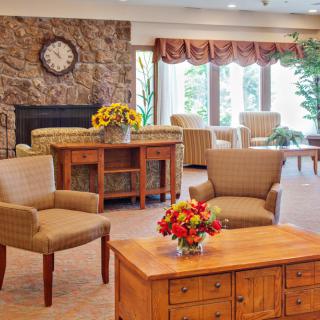 A cozy living room interior featuring comfortable seating, a wooden coffee table with floral arrangement, and large windows letting in natural light.