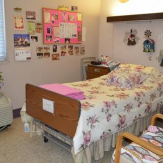 A decorated room with a hospital bed, floral bedding, and photographs on the wall.