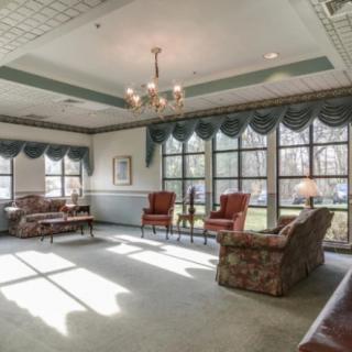 A spacious living room with large windows, featuring a chandelier, armchairs, and a patterned sofa.