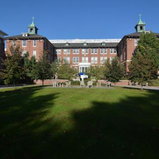 A historic academic building surrounded by lush greenery on a sunny day.