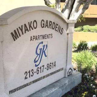 Sign for Miyako Gardens Apartments with contact information.