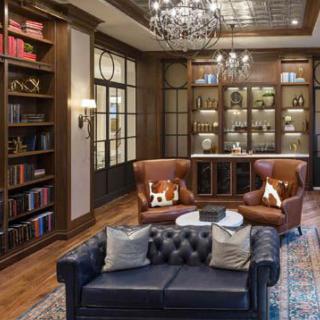 A luxurious library with elegant armchairs, a leather sofa, and well-stocked bookshelves under a grand chandelier.