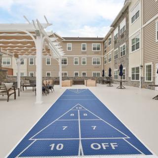 An outdoor shuffleboard court surrounded by a residential building and patio seating.