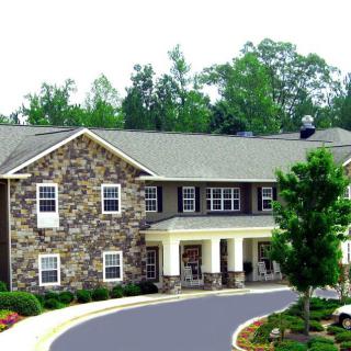 A two-story stone house with a driveway and surrounding greenery.
