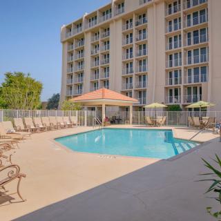 An outdoor swimming pool area with lounge chairs and a canopy beside a multi-story hotel building.