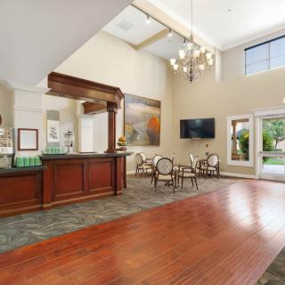 A spacious hotel lobby with a reception desk, chandelier, seating area, and wood flooring.
