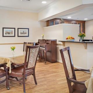 A cozy dining area with a piano, tables, and chairs on a wooden floor.
