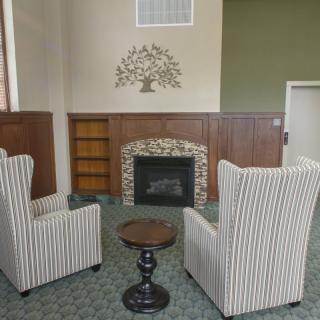 A cozy living room with two striped chairs facing a small table and a fireplace, adorned with wall decor.