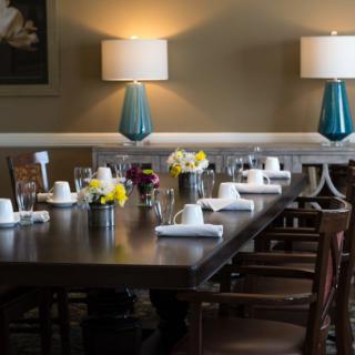A dining room table elegantly set with flowers, surrounded by wooden chairs and illuminated by warm lamps.