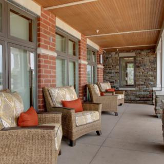 A cozy porch with wicker chairs and cushions, surrounded by brick walls and featuring large windows.