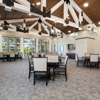 A modern dining area with tables and chairs, featuring large windows and exposed ceiling beams.