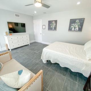 A modern, minimalist bedroom featuring a bed, dresser, and wall-mounted TV.