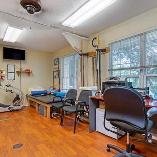 A therapy room with exercise equipment, chairs, desks, and large windows.
