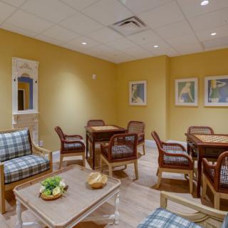 A cozy waiting room furnished with plaid-upholstered chairs and tables, decorated with framed artwork on yellow walls.