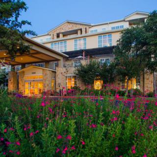 A hotel building surrounded by vibrant flowers and trees in the evening.