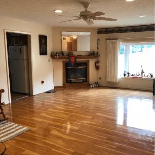 Spacious living room with hardwood flooring, a fireplace, ceiling fan, and a window seat.