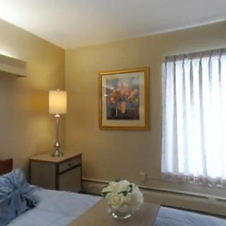 A cozy bedroom with a lamp, artwork, and a window letting in natural light.