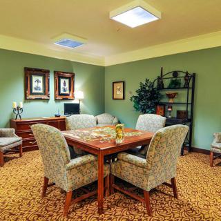 A cozy living room with a central table surrounded by upholstered chairs, complemented by wall art and a bookshelf.