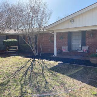 A cozy brick house with a well-maintained front yard and porch on a sunny day.