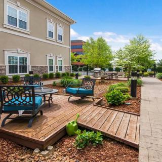 A modern outdoor seating area with a wooden deck surrounded by greenery and adjacent to a building.