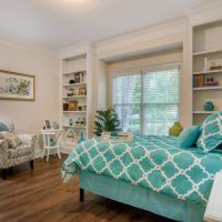 A cozy bedroom with a teal-themed decor, featuring a bed, shelves, and a large window.