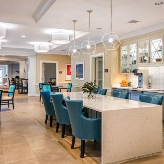 A modern dining and kitchen area with blue upholstered chairs and a sleek marble countertop, illuminated by chandelier lighting.