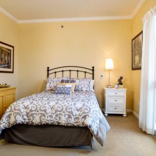 A cozy bedroom with a metal-framed bed, patterned bedding, and a nightstand with a lamp.
