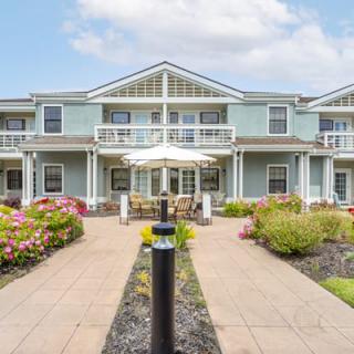 A picturesque residential building with symmetrical architecture, surrounded by well-maintained landscaping and a central pathway.