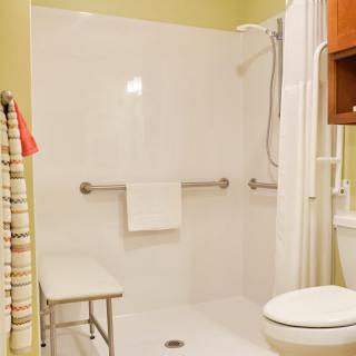 A bathroom featuring an accessible shower with grab bars and a bench.